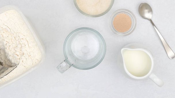 Dry yeast, milk, sugar, flour. Close up baking process, ingredients for baking needs on kitchen table - Photo, Image