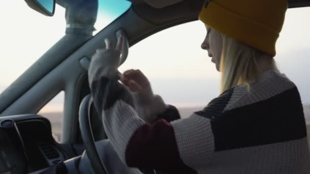 Young woman in a yellow hat sits in car and poses on camera - Footage, Video