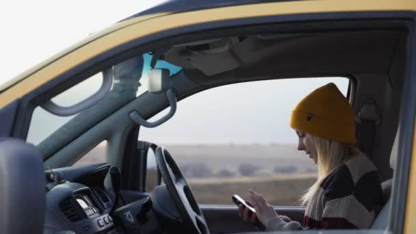 Young woman in a yellow hat sits in car and uses phone - Footage, Video