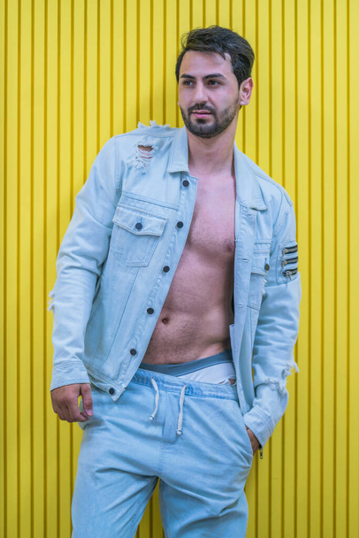 portrait of caucasian strong man model posing in jean with yellow wall background - Photo, image