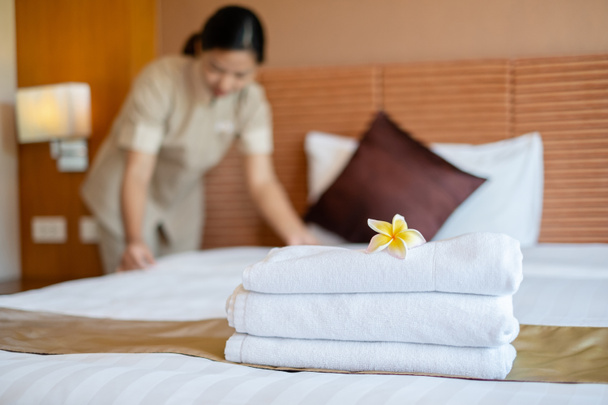 ホテルのメイドがベッドにタオルを積み、ホテルの部屋にタオルに花を置きました。. - 写真・画像