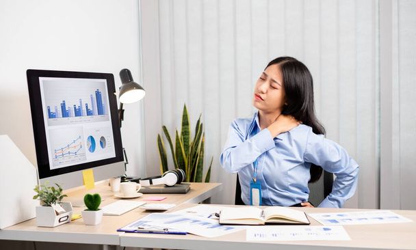 Aziatische vrouwelijke accountant is moe van het werken in een stoel, rekken om te ontspannen en te ontspannen tijdens het werken hard op kantoor. - Foto, afbeelding
