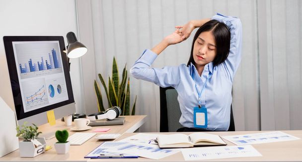 Asian female accountant is tired from working in a chair, stretching to relax and relax while working hard at the office. - Photo, Image