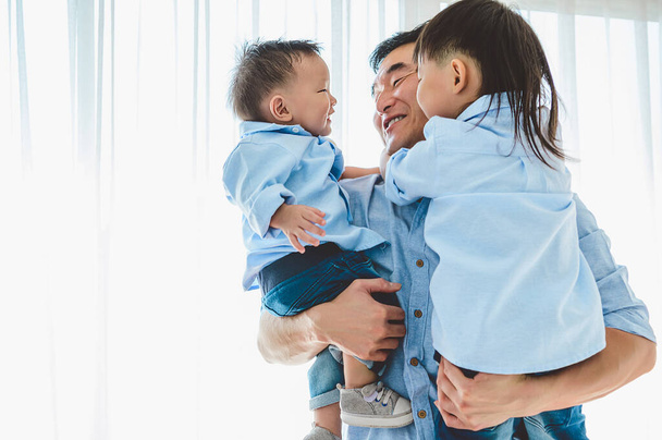 Ευτυχισμένος πατέρας κουβαλάει δύο παιδιά στην κρεβατοκάμαρα στο σπίτι. Ασιατική οικογένεια που ζουν και έχουν έκφραση προσώπου μαζί. Ελεύθερος χρόνος. Υγεία των ανθρώπων. Θεματικό θέμα του ιού του καραντίνου Covid-19 Coranavirus - Φωτογραφία, εικόνα