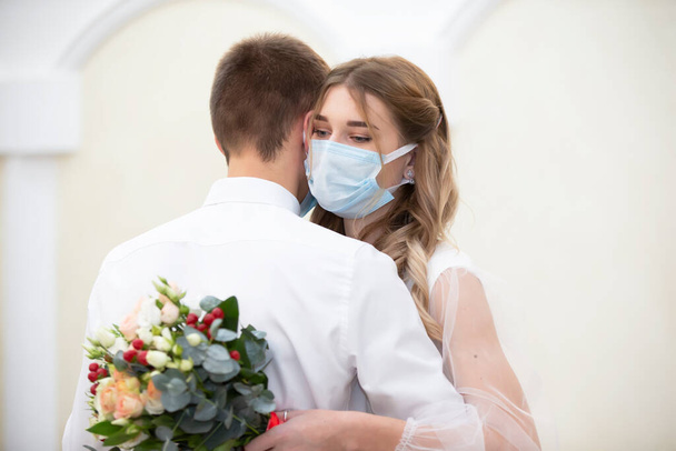 The bride in a medical mask with a bouquet of flowers is dancing with the groom. Wedding during the coronavirus panademia. - Photo, Image