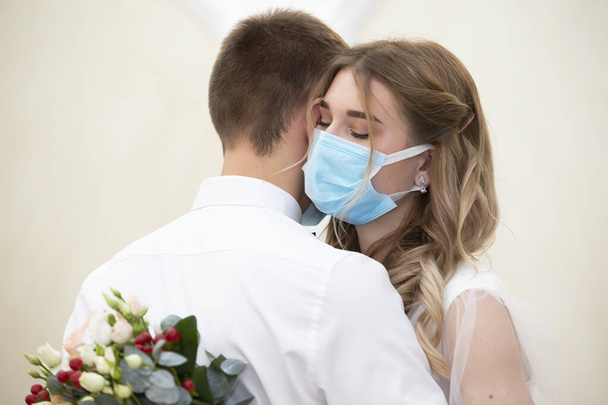 De bruid in een medisch masker met een boeket bloemen danst met de bruidegom. Bruiloft tijdens de coronavirus panademie. - Foto, afbeelding