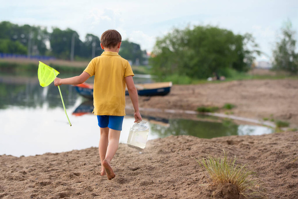 Ein kleiner Junge mit einem Fischernetz geht am Ufer des Sees entlang. - Foto, Bild
