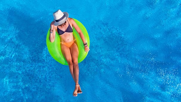 Beautiful woman in hat in swimming pool aerial view from above, young girl relaxes and has fun on inflatable ring in water on vacation - Photo, Image