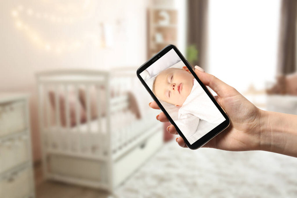 Мати використовує сучасний мобільний телефон як дитячий монітор вдома
 - Фото, зображення