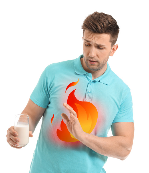 Young man with glass of milk suffering from heartburn on white background - Photo, Image