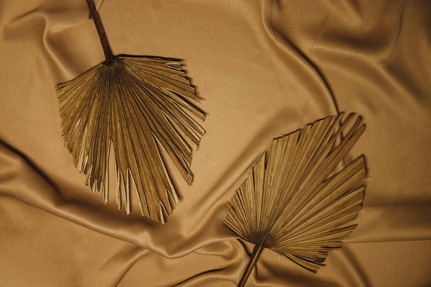 On the folds of the beige fabric are dry palm leaves. Natural and fashionable colors.Trend of the year.Background and texture. - Фото, изображение