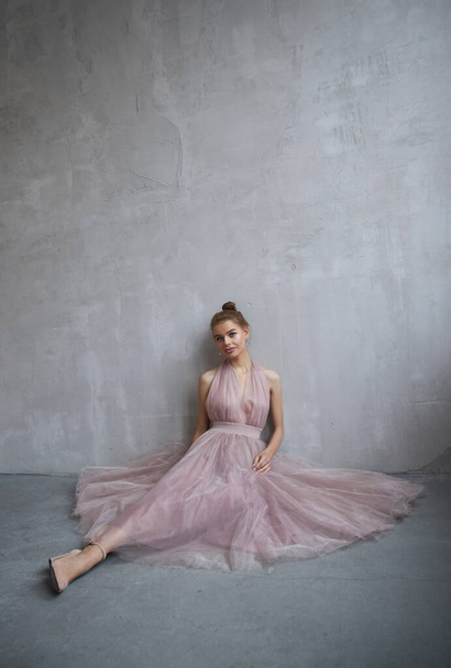 Fashion beautiful woman in a dress sitting on the floor against the wall. Perfect makeup, romantic portrait - Photo, image