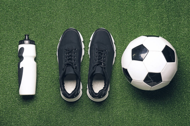 Sportieve schoenen, voetbal en fles water op kleur achtergrond - Foto, afbeelding