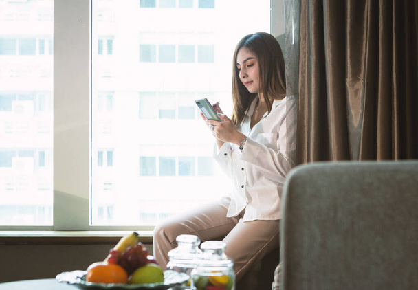 Práce z domova koncept: Krásná asijská žena pomocí smartphone při práci v obývacím pokoji - Fotografie, Obrázek