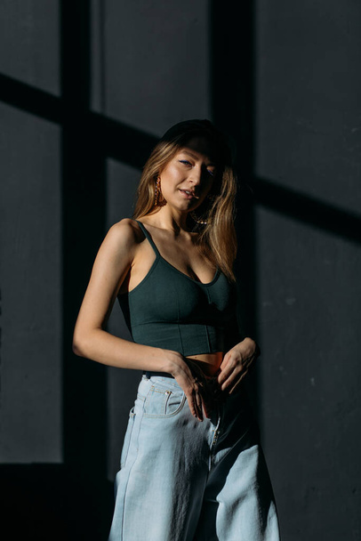 young beautiful girl with dyne loose hair in a top and jeans in the studio on a black background in the rays of the sun - 写真・画像