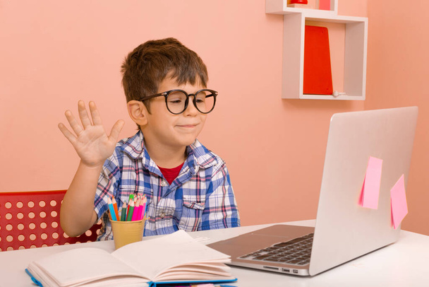 Uczenie się dzieci w domu poprzez wirtualne zajęcia. Interaktywne treści do podstawowej klasy online. Nauka w domu. Chłopiec ze słuchawkami za pomocą laptopa przy stole w pokoju - Zdjęcie, obraz