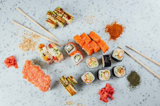 Vista de cerca de una variedad de comida japonesa de sushi y rollos en mesa brillante, palillos e ingredientes  - Foto, imagen
