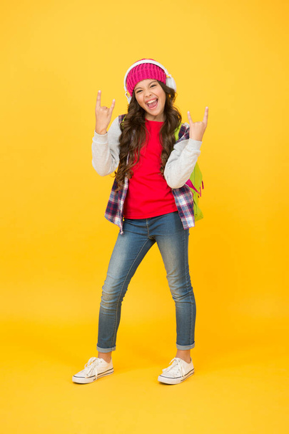 Happy girl show rock horn signs listening to music in modern headphones in casual fashion style yellow background, cool - Foto, afbeelding