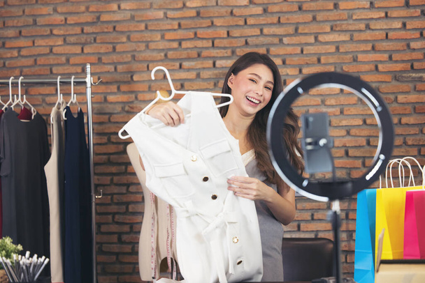 Азиатская молодая женщина в прямом эфире для продажи модной одежды представляет блоггер для социальных людей. Ее влияние в социальной сети. - Фото, изображение