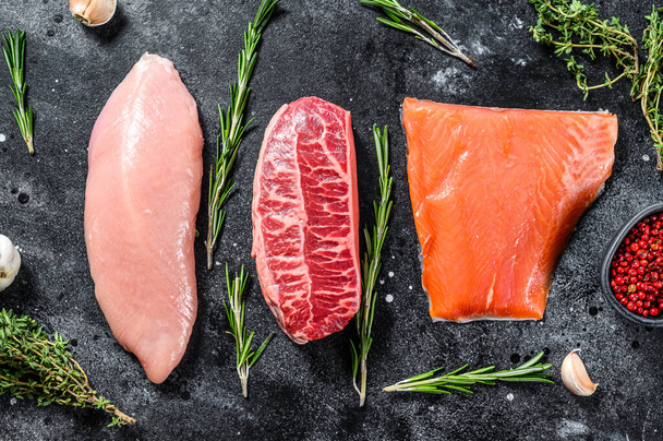 Different types of raw meat with herbs. Beef top blade, salmon fillet and Turkey breast. steaks. Black background. Top view. - Φωτογραφία, εικόνα