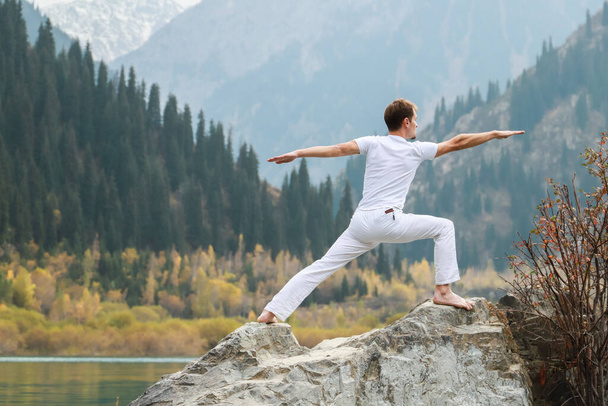A man practices yoga on a background of mountains. Pose Virabhadrasana 2 or warrior - Фото, изображение