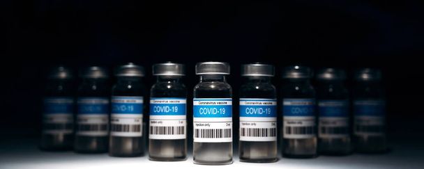 Foto panorámica de muchas ampollas con la vacuna contra el virus de la corona COVID-19 para inyección sobre fondo negro. Fabricación de vacunas contra el Coronavirus, vacunación mundial y concepto sanitario - Foto, imagen