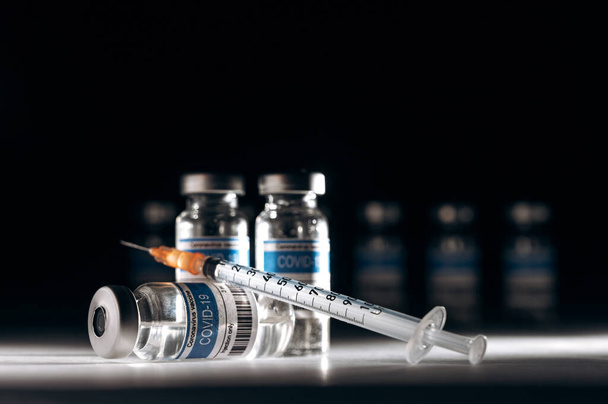Ampolas médicas com uma vacina contra o coronavírus e uma seringa em laboratório sobre um fundo preto. COVID-19 vacinação mundial. Conceito de medicina e prevenção da saúde - Foto, Imagem