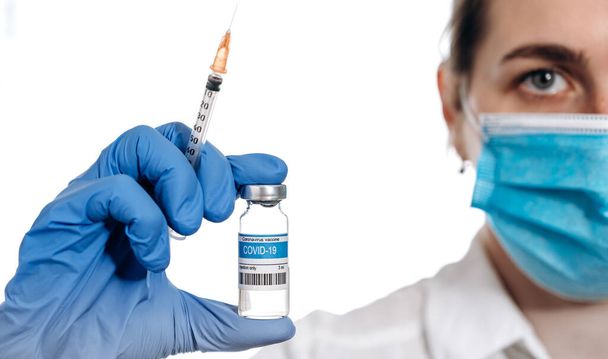 Close-up ampul met COVID-19 vaccin en spuit in de hand van een vrouwelijke arts. Corona virus vaccin voor COVID. Concept van geneeskunde, trial en behandeling als gevolg van SARS-CoV-2 coronavirus - Foto, afbeelding