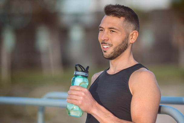 El hombre bebe agua con limón de la botella reutilizable durante un entrenamiento. Beber mientras se hace ejercicio. Deshidratación durante el entrenamiento - Foto, imagen