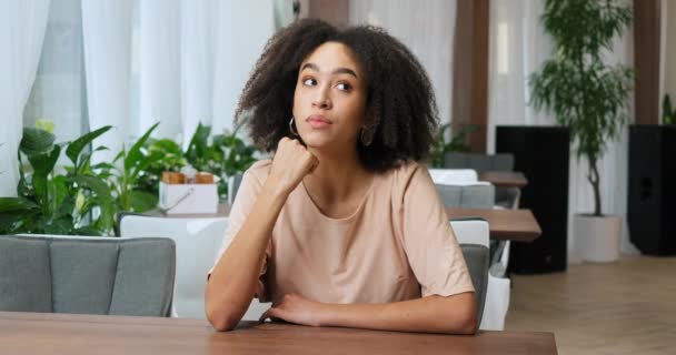 Güzel, duygusal, düşünceli, Afro-Amerikan bir kadının portresi, kıvırcık saçlı, kafeteryada oturuyor, seçimler yapıyor, anıları anımsıyor, fikirler hakkında düşünüyor, kaşlarını çatan bir gelecek sunuyor. - Video, Çekim