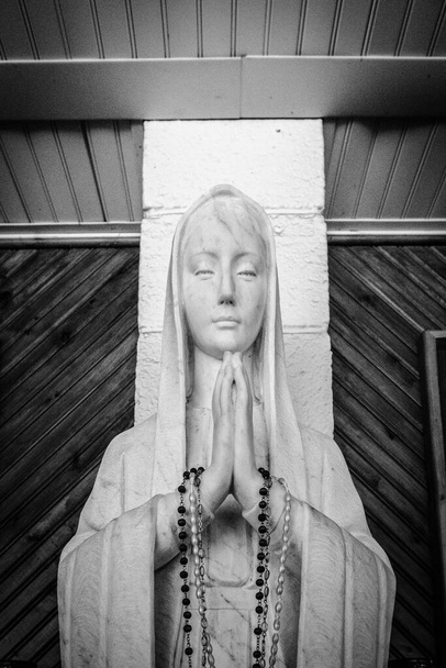 Η Παρθένος Μαρία. Άγαλμα της Παναγίας προσεύχεται με κομπολόι χάντρες στα χέρια της. Ασπρόμαυρο σε κάθετο προσανατολισμό. - Φωτογραφία, εικόνα