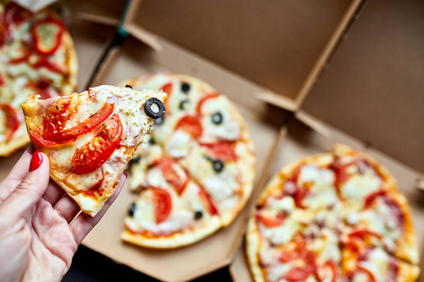 Female hands takes a slice of delicious pizza from a delivery box on a black table - Фото, изображение