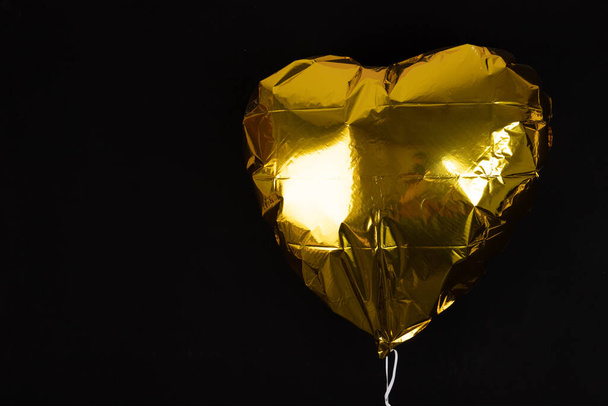 Golden heart shaped balloon, on black background, with copy space - Foto, afbeelding