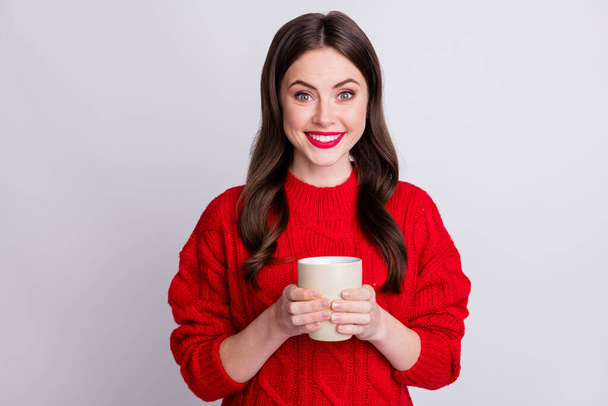 Photo portrait of happy smiling girl keeping cup with hot tea wearing red knitted pullover happy isolated on pastel grey color background - Фото, изображение
