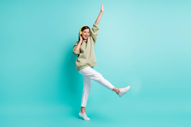 Full length photo portrait of cool woman wearing green headphones dancing standing on one leg isolated on vivid turquoise colored background - Photo, Image