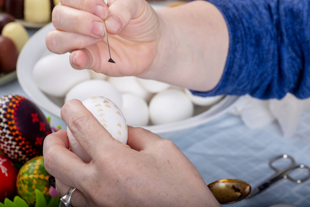 Les mains féminines peignent un œuf de Pâques blanc selon la tradition sorabe avec une plume d'oie parée et de la cire de bougie fondue. - Photo, image