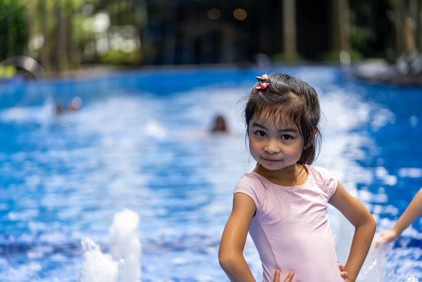 Retrato de un niño bastante asiático oliendo y posando en el fondo de la piscina con traje de baño rosa - Foto, imagen