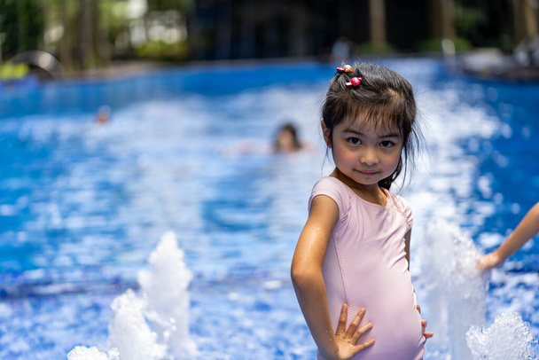 Retrato de un niño bastante asiático oliendo y posando en el fondo de la piscina con traje de baño rosa - Foto, imagen