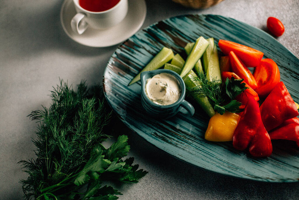 platter with fresh chopped vegetables and sauce with tea cup on table, close view  - Photo, Image