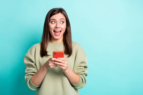 Photo portrait of amazed screaming woman holding phone in two hands looking at blank space isolated on vivid turquoise colored background - Foto, imagen