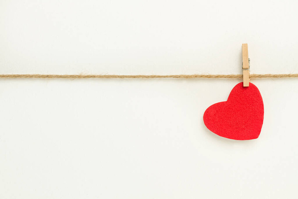 Μια κόκκινη χάρτινη καρδιά κρέμεται από ένα νήμα σιζάλ σε λευκό φόντο - Φωτογραφία, εικόνα