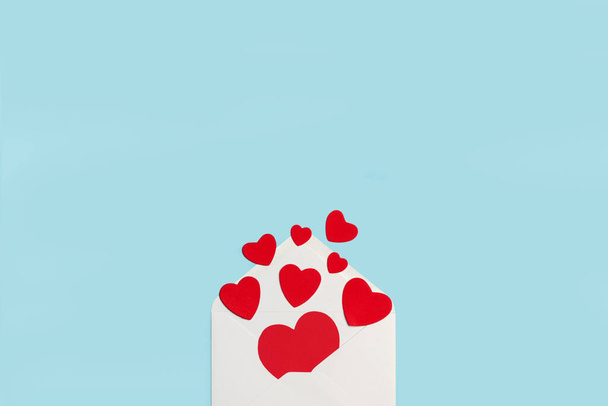 Красные бумажные сердечки на белом конверте и на голубом фоне - Фото, изображение