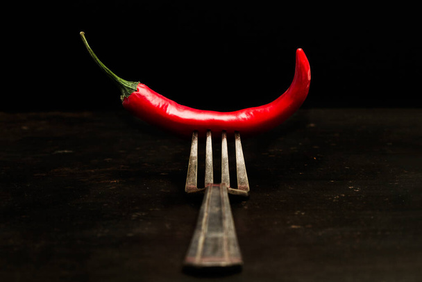 Червоний гострий перець чилі і виделка на металевому столі на темному фоні
 - Фото, зображення