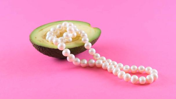 Fruit d'avocat à moitié frais avec des perles sur un fond rose. Design alimentaire à la mode. - Photo, image