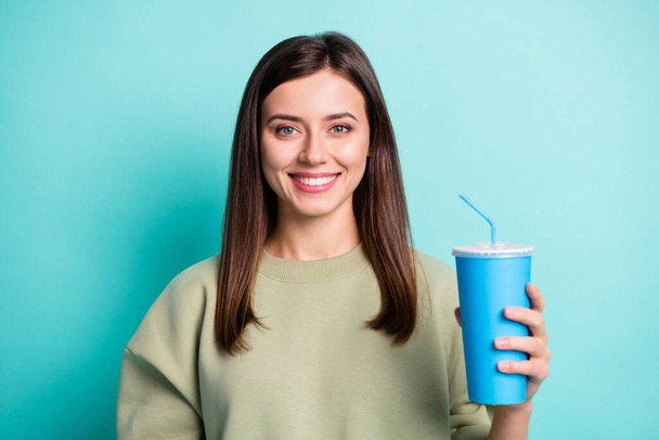 Photo portrait of girl holding blue plastic cup of soda in one hand isolated on vivid cyan colored background - Fotó, kép