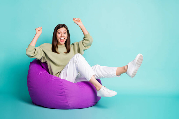 Photo portrait full body view of woman raising two legs and arms celebrating sitting in purple chair isolated on vivid teal colored background - Foto, Bild