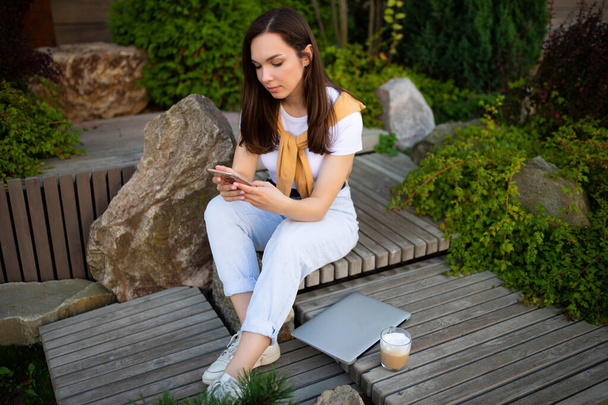 affascinante giovane donna libera in look casual sta bevendo caffè mentre seduto in un parco estivo - Foto, immagini