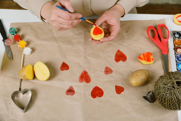 heart shaped potato stamp on craft paper. The process of decorating a gift for Valentines Day. Getting ready for the celebration on February 14th. - Фото, изображение