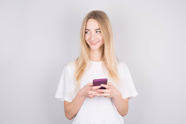 Photo of cheerful cute beautiful young woman chatting by mobile phone isolated over white wall. Looking aside to copyspace. - Foto, Imagem