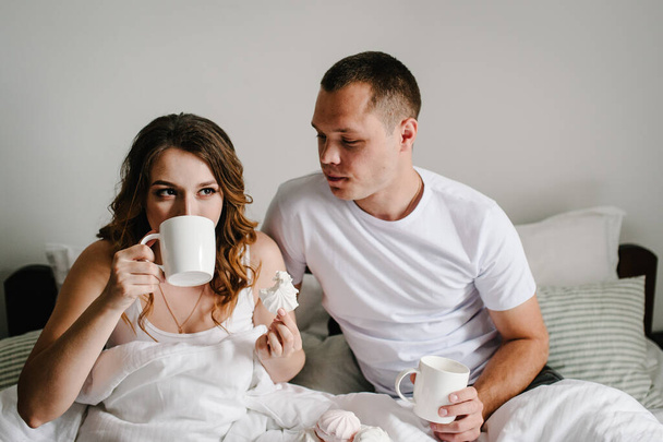 A man and a woman drink coffee and eat marshmallows in bed, in bedroom. The Valentine's Day Concept. Celebrating holiday. Lifestyle. Women's Day, eighth of March. Close up. Emotions of happiness. - Φωτογραφία, εικόνα